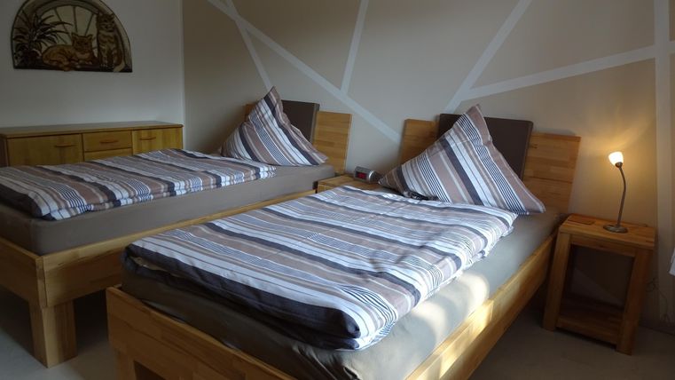 Een gezellige kamer met twee eenpersoonsbedden en een modern houten ontwerp. De ruimte heeft een warme sfeer en eenvoudige verlichting.