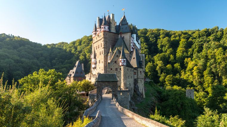 Burg Eltz mit Brücke und Wald im Hintergrund.