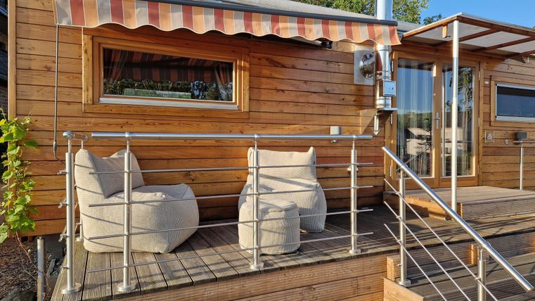 Ein gemütliches Holzhaus mit einem Außenbereich. Vor dem Haus stehen zwei bequeme Sessel auf der Terrasse.