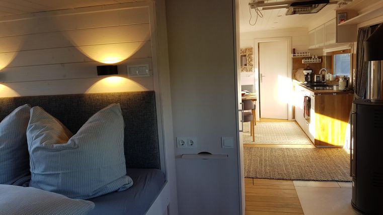 Ein gemütlicher Raum mit einer gemütlichen Sitzgelegenheit und einer modernen Küche im Hintergrund. Das Licht sorgt für eine einladende Atmosphäre.