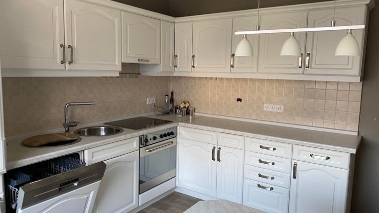 Eine helle moderne Küche mit weißen Schränken und Edelstahlgeräten. Der Raum ist gut beleuchtet und bietet eine praktische Anordnung von Arbeitsflächen.