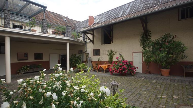 Ein einladender Innenhof mit Blumen und Bänken. Umgeben von traditionellen Gebäuden und grünem Pflanzenbewuchs.