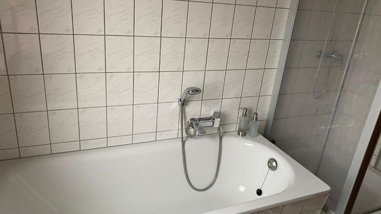 Ein Badezimmer mit einer weißen Badewanne und einer modernen Dusche. Die Wände sind mit hellen Fliesen gestaltet.