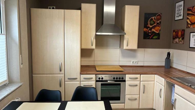 Eine moderne Küche mit hellen Holzschränken und Edelstahl-Geräten. Der Tisch ist mit Platzsets gedeckt und es gibt einige Wandbilder.