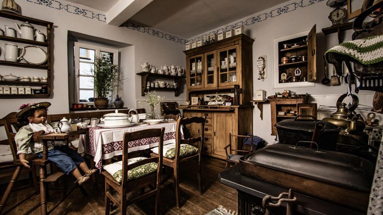 Eine traditionelle Küche mit Holzmöbeln und einem großen Esstisch. Im Hintergrund sind Geschirr und Dekorationen zu sehen.