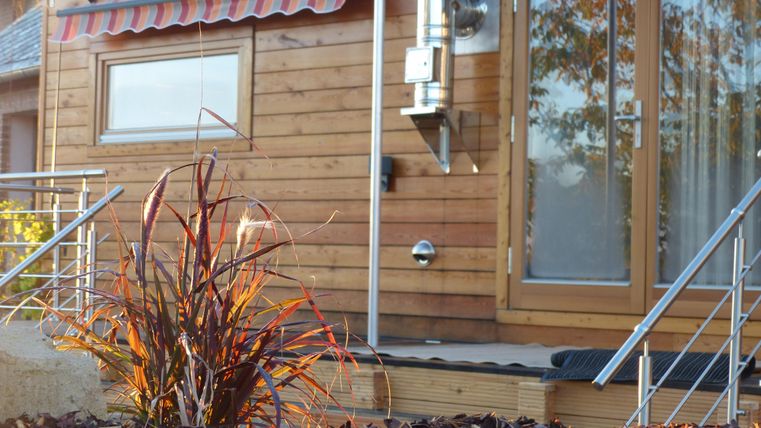 Ein modernes Holzhaus mit großen Fenstern und einem einladenden Eingang. Vor dem Haus wächst eine attraktive Pflanze in einer Mulchschicht.