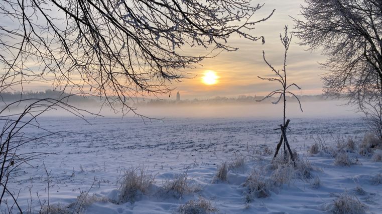 Im Hintergrund geht die Sonne unter, im Vordergrund eine Landschaft im Schnee