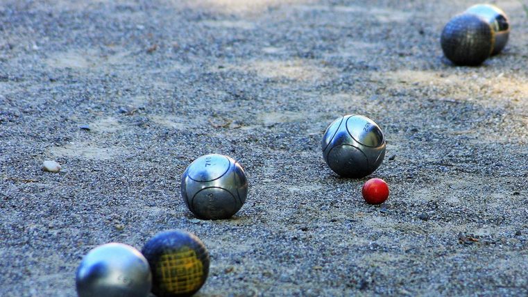 Eine Boule-Bahn mit mehreren Kugeln im Sand. Eine rote Kugel liegt in der Nähe der silbernen Kugeln.