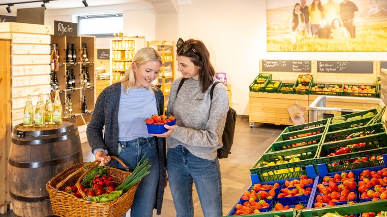 Zwei Frauen betrachten Erdbeeren beim Einkauf im Hofladen Adams.