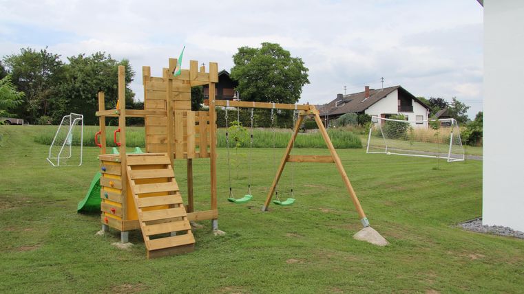 Un beau terrain de jeu en bois avec un toboggan, une structure d'escalade et deux balançoires. La pelouse verte offre beaucoup d'espace pour jouer.