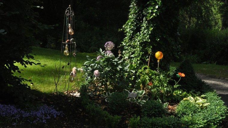 Ein schöner Garten mit verschiedenen Pflanzen und Blumen. Es gibt auch einige dekorative Elemente und Schatten von Bäumen.