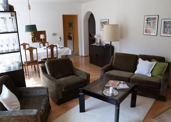 Ein modernes Wohnzimmer mit bequemen Sofas und einem gläsernen Tisch. Im Hintergrund befindet sich ein Essbereich mit einem Tisch und Stühlen.