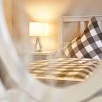 Ein gemütliches Schlafzimmer mit einem karierten Kissen und einer sanften Lampe. Das warme Licht schafft eine einladende Atmosphäre.