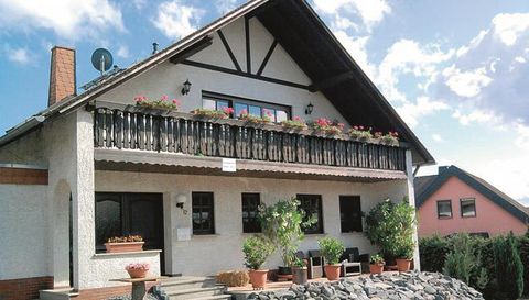 Ein charmantes Haus mit einem Balkon und bunten Blumen. Die Umgebung ist grün und einladend.