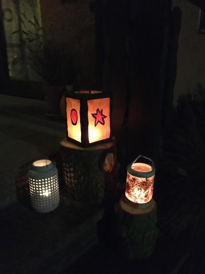 Twee stralende lantaarns met kleurrijk papier in rood- en oranjetinten. Ze staan op een rooster en stralen warm licht uit.