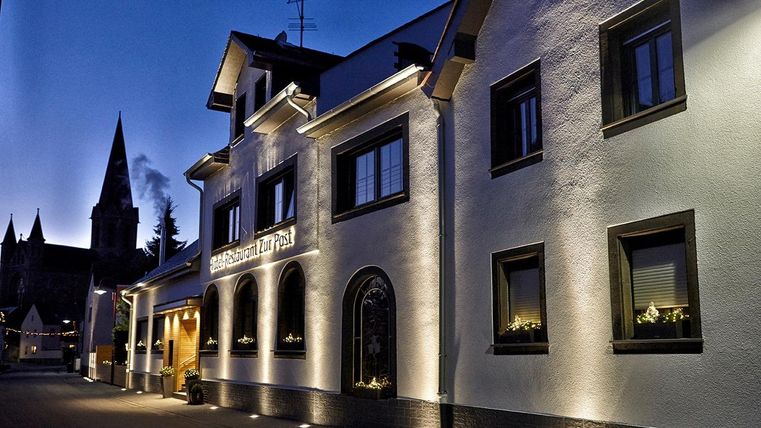 Ein hübsches Gebäude mit moderner Beleuchtung in der Abenddämmerung. Im Hintergrund ist ein Kirchturm sichtbar.