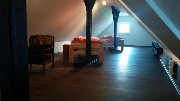 Ein gemütlicher Dachboden mit Holzfußboden und niedriger Decke. Es gibt ein Bett und eine Sitzgelegenheit in der Ecke.